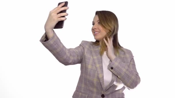 Sonriente mujer rubia feliz en chaqueta haciendo selfie en el teléfono inteligente sobre fondo blanco — Vídeos de Stock