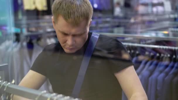Jonge aantrekkelijke man te kijken naar etalage met mens past in het winkelcentrum — Stockvideo