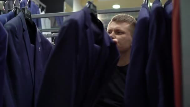 Shopping and fashion concept - Young man choosing and trying jacket on in mall or clothing store — Stock Video