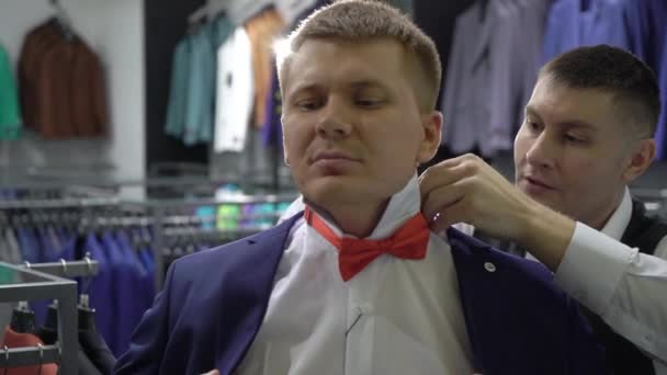 Compras y concepto de moda - Hombre joven elegir y probar chaqueta en el centro comercial o tienda de ropa — Vídeo de stock