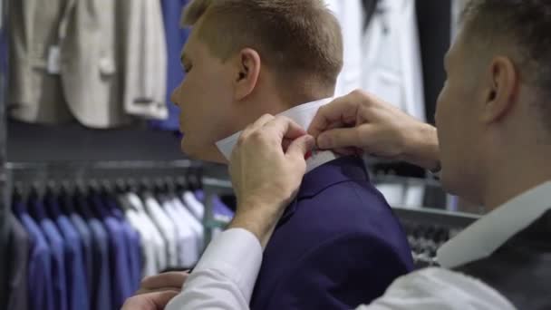 Compras y concepto de moda - Hombre joven elegir y probar chaqueta en el centro comercial o tienda de ropa — Vídeo de stock