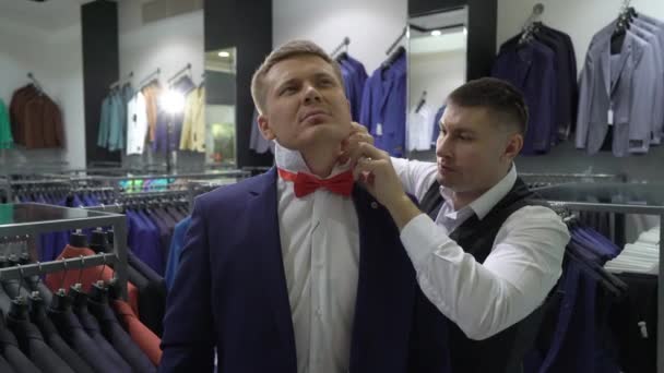 Zakupy i koncepcja mody-młody człowiek wybiera i próbuje Kurtka na w centrum handlowym lub Sklep odzieżowy — Wideo stockowe