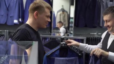 Alışveriş ve moda konsepti-genç adam seçimi ve alışveriş merkezi veya giyim mağazasında ceket çalışıyor