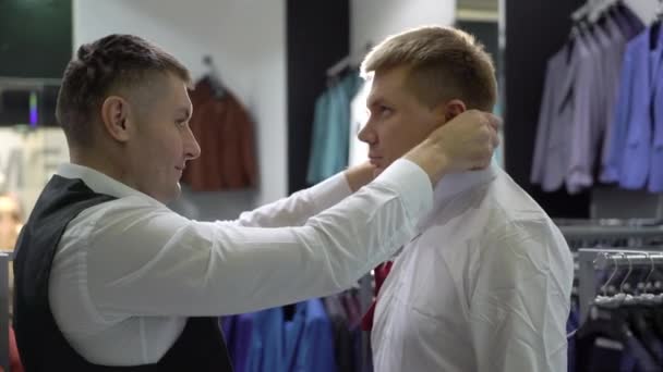 Концепция шопинга и моды - молодой человек выбирает и примеряет куртку в магазине одежды — стоковое видео