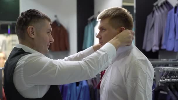 Compras y concepto de moda - Hombre joven elegir y probar chaqueta en el centro comercial o tienda de ropa — Vídeo de stock