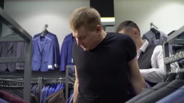 Alışveriş ve moda konsepti-genç adam seçimi ve alışveriş merkezi veya giyim mağazasında ceket çalışıyor