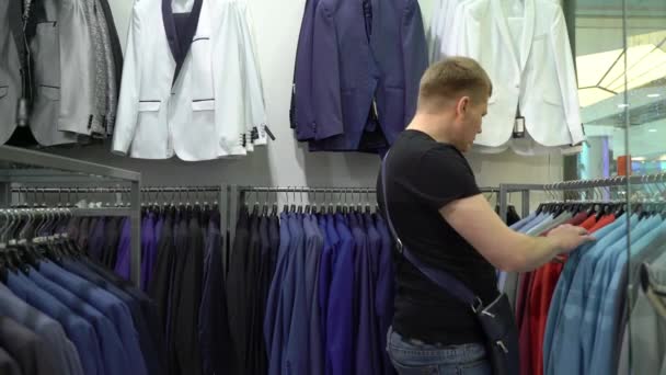 Winkelen en mode concept - jonge man kiezen en proberen jas op in mall of kledingwinkel — Stockvideo