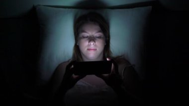 Gece uyuyan önce yatakta cep telefonu kullanan genç kadın. Mobil bağımlısı kavramı.