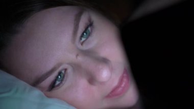 Gece uyuyan önce yatakta cep telefonu kullanan genç kadın. Mobil bağımlısı kavramı.