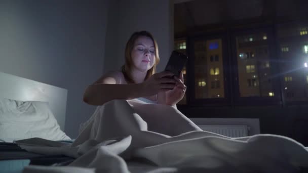 Młoda kobieta za pomocą telefonu komórkowego na łóżku przed snem w nocy. Mobilna koncepcja addict. — Wideo stockowe