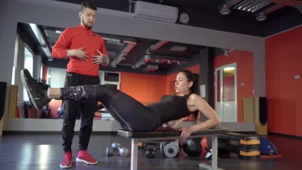 Joven saludable deportista activa forma chica con un guapo entrenador personal útil junto a ella en el gimnasio . — Vídeos de Stock