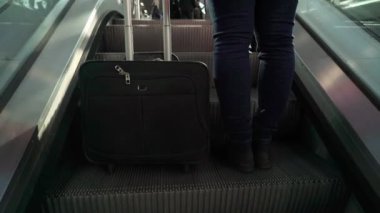 Yürüyen merdivene yürüyen bir bavul ile genç kadın