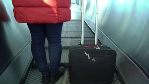 Yürüyen merdivene yürüyen bir bavul ile genç kadın — Stok video