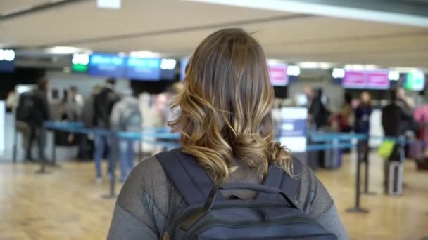 Перед вылетом в аэропорту стоит женщина-путешественница. Девушка с рюкзаком в аэропорту — стоковое видео