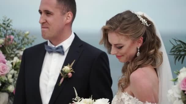 Gli sposi alla cerimonia nuziale. Una giovane coppia innamorata si trova all'arco. Matrimonio al mare — Video Stock