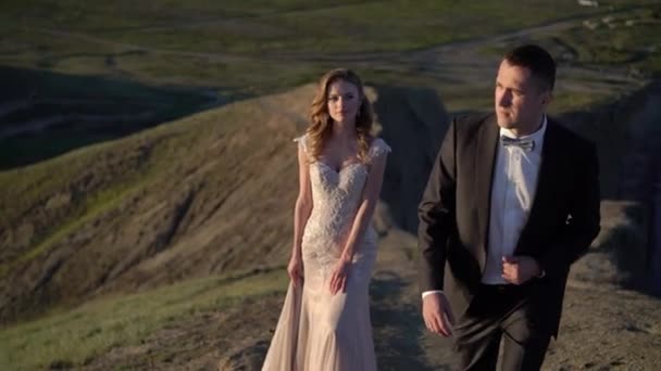 Жених и невеста гуляют по горам на закате — стоковое видео