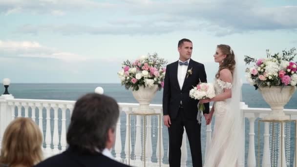 A noiva e o noivo na cerimónia de casamento. Um jovem casal apaixonado está no arco. Casamento junto ao mar — Vídeo de Stock