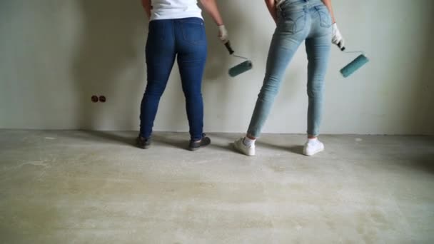 Dos trabajadoras que usan rodillo para pintar las paredes del apartamento o casa. Construcción, reparación y renovación . — Vídeo de stock