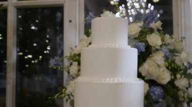 Göz kamaştırıcı beyaz bir düğün pastası çiçek aranjmanları ve ışıl ışıl bir avizeyle zarif bir şekilde sergileniyor..