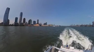 İkonik New York siluetinin berrak gökyüzüne ve sakin bir su ön planına karşı çarpıcı panoramik görüntüsü.