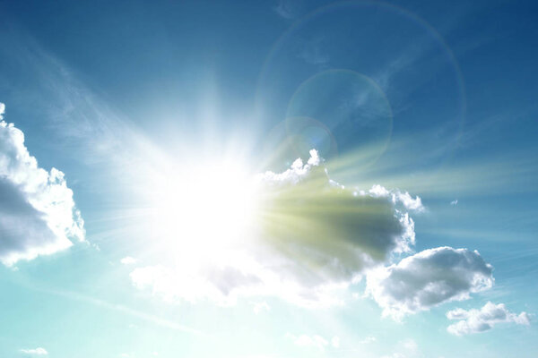 Sun high in the sky with rays sprouting in front of clouds 