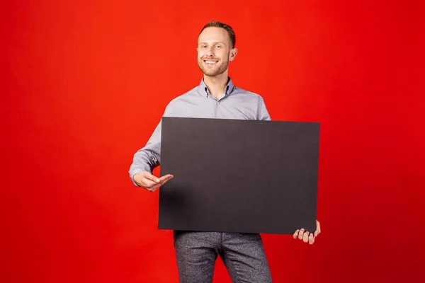 Молодой человек держит черную панель с местом для текста на красной подложке — стоковое фото
