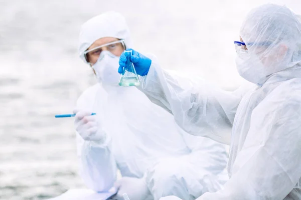 Ecologistas vestindo uniformes protetores examinando o líquido cont — Fotografia de Stock