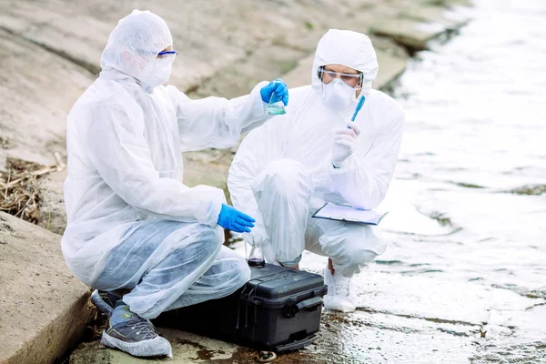 Ecologisti che indossano uniformi protettive esaminando il contenuto liquido — Foto Stock