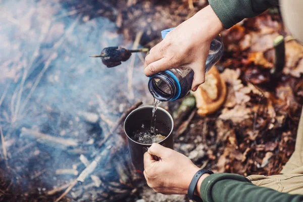 Jäger gießt Wasser aus Flasche in Metallbecher. — Stockfoto