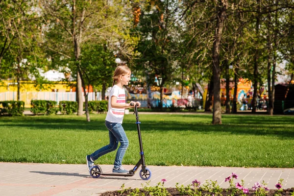 Flicka rida en skoter i en stadspark på soliga sommardagen. Aktiva — Stockfoto