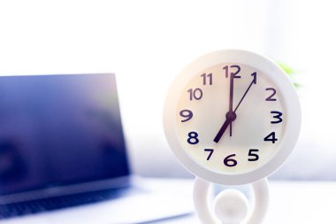 Sabah güneşinde, dizüstü bilgisayarlı beyaz bir saat.