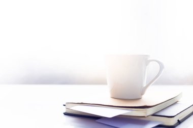 Sabah güneşinde beyaz masada, defterin üzerinde kahve, çalışma alanı.