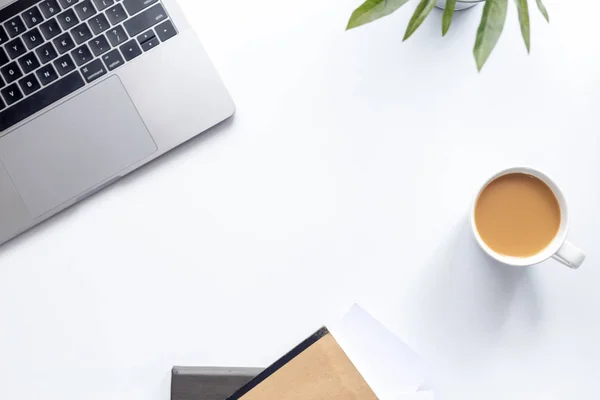 Üst görünüm çalışma alanı, beyaz masadaki dizüstü bilgisayar kahve fincanı ve arka plandaki not defteri.