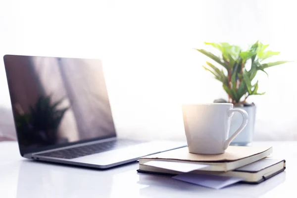 Defter üzerinde kahve ile sabah güneş ışığı, çalışma alanı içinde beyaz masa üstünde laptop