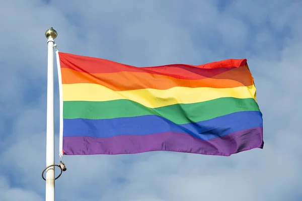 Rainbow Flag waving in the wind with a partly cloudy sky.