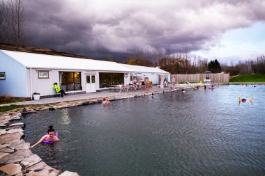 FLUDIR, ICELAND OCTOBER 11, 2018: People bathing in geothermal pools of Secret Lagoon. Secret lagoon hot spring, public outdoor warming swimming pool. clipart