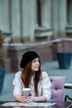 Açık havada moda portre gitmek için kahve içme genç güzel kız. Holding bir gülümseyen kız portresi yakından açık havada kahve fincanı götürün.