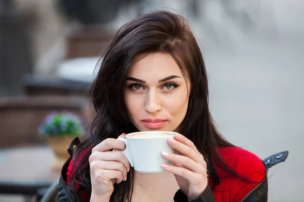 Outdoors fashion portrait of young beautiful girl drinking coffee.Close up portrait of a smiling young girl holding take away coffee cup outdoors.Young stylish woman drinking coffee in a city street