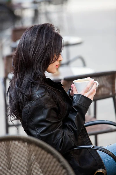 Gorgeous young woman with cup of coffee in city street. Coffee break. Stylish hipster girl drinking coffee in street.Outdoors fashion portrait of young beautiful girl drinking coffee.