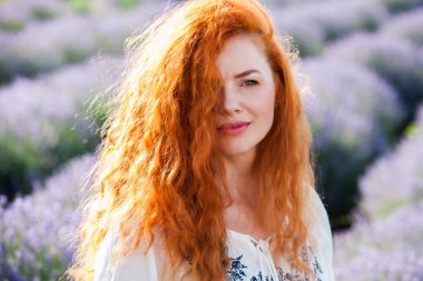 Uzun kıvırcık kızıl saçlı güzel bir kızın yaz portresi. Uzun saçlı kadın. Lavander alanında Avrupalı kız.