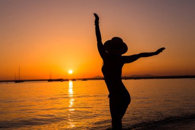 Gün batımı, seksi kadın silueti. Tasasız kadın sahilde gün batımının tadını çıkarıyor. Mutlu bir yaşam tarzı. Mallorca. Es Prenc plajı.