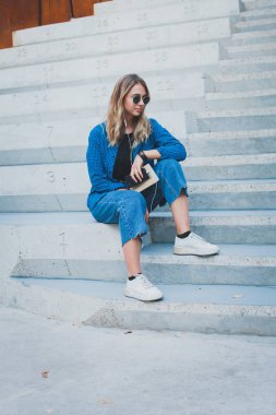 Mutlu bir kız bir yaz güneşli bir günde sokakta bir akıllı telefon kulaklık ile hat müzik dinlerken portresi. Telefonla müzik dinleyen ve eğlenen kadın