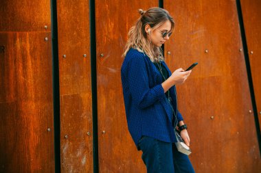 Mutlu bir kız bir yaz güneşli bir günde sokakta bir akıllı telefon kulaklık ile hat müzik dinlerken portresi. Telefonla müzik dinleyen ve eğlenen kadın