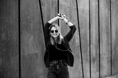 Mutlu bir kız bir yaz güneşli bir günde sokakta bir akıllı telefon kulaklık ile hat müzik dinlerken portresi. Telefonla müzik dinleyen ve eğlenen kadın