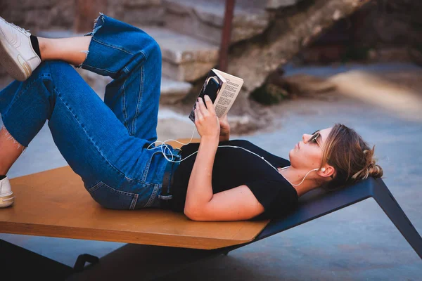 Young girl reading a book in the street.  female hipster enjoying literature outdoors. Smiling teen girl dressed in casual reading book.