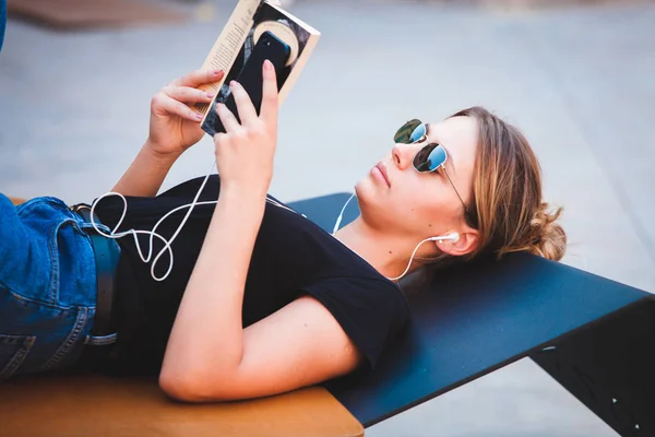 Young girl reading a book in the street.  female hipster enjoying literature outdoors. Smiling teen girl dressed in casual reading book.