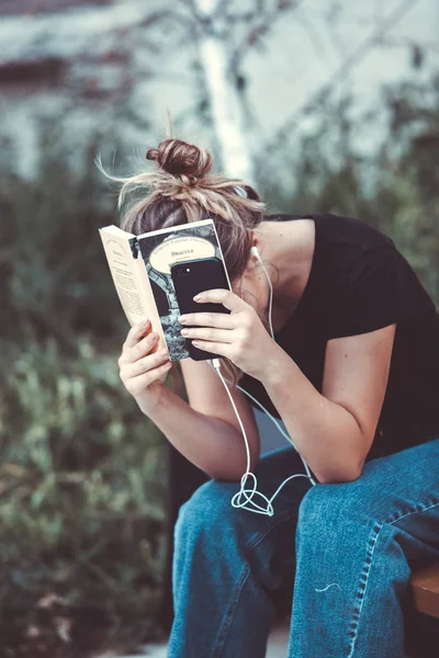 Young girl reading a book in the street.  female hipster enjoying literature outdoors. Smiling teen girl dressed in casual reading book.