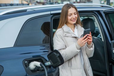 Genç bir iş kadını elektrikli arabasına EV şarj istasyonunda yakıt ikmali yapıyor. Çevre dostu araç kavramı. Elektrikli araba konsepti. Yeşil seyahat.