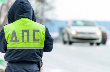 Russian police patrol Inspectorate regulate traffic on city street. Inspector of traffic policein yellow vest jacket with a Russian inscription on the back of the uniform jacket 