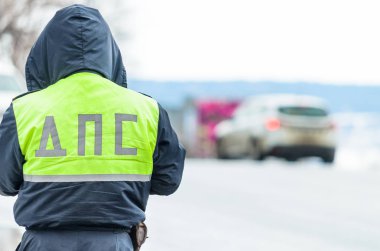 Russian police patrol of the State Automobile Inspectorate regulate traffic on city street. Inspector of traffic policein yellow vest jacket with a sign 